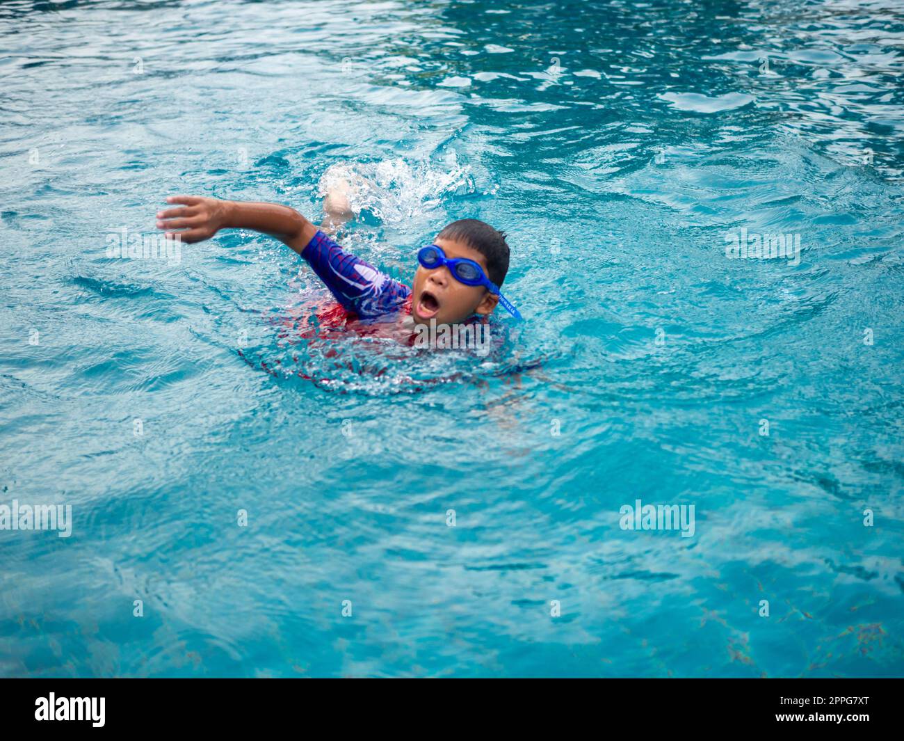 garçon portant un maillot de bain et des lunettes nageant au milieu de la piscine avec un fond bleu Banque D'Images