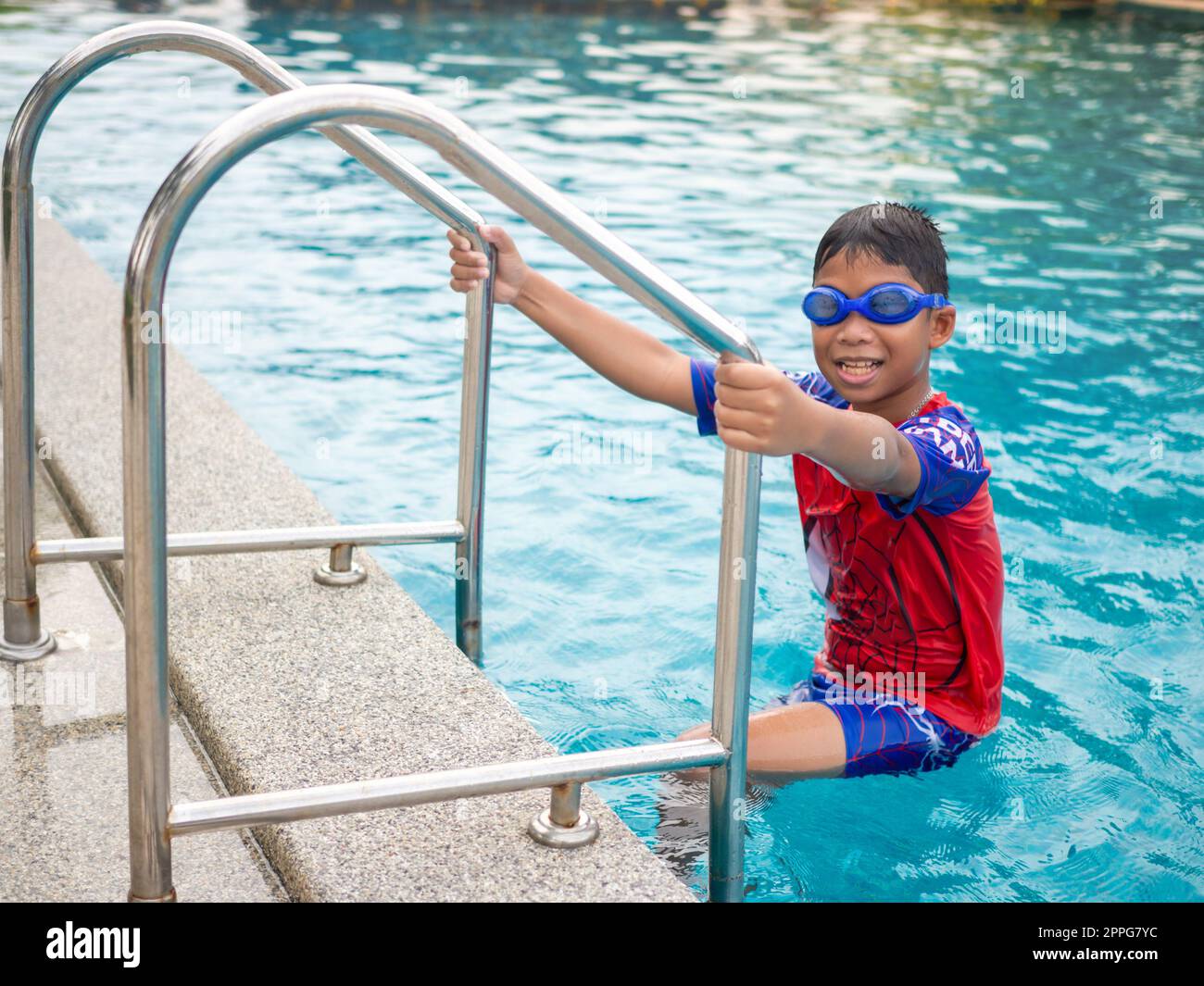 Le garçon portant des lunettes de natation sur l'échelle bleue de piscine rouge maillot de bain Banque D'Images