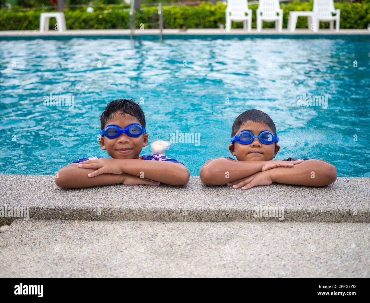 Les frères portant des maillots de bain et des lunettes se sourient tout en étant perchés au bord de la piscine. Banque D'Images