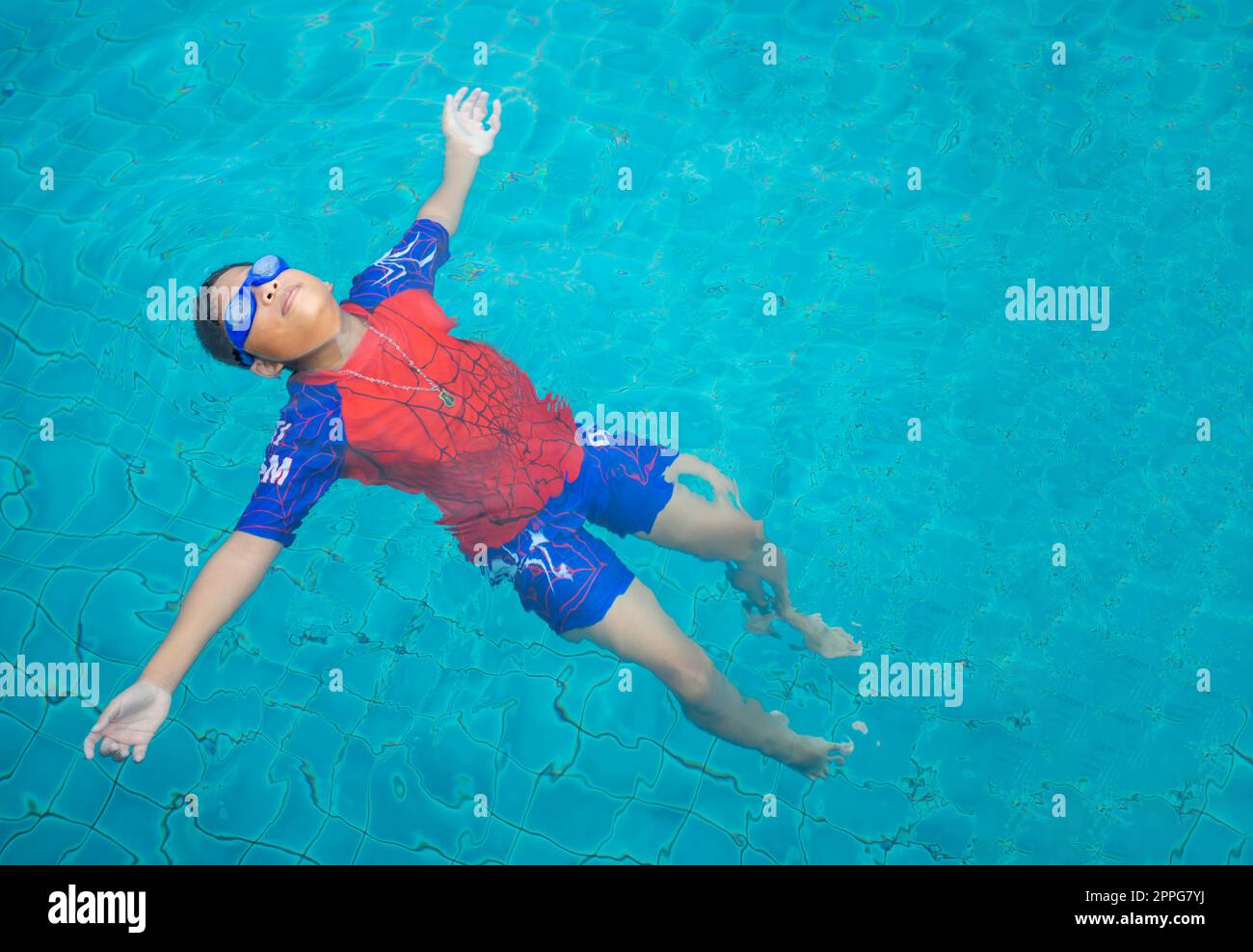 garçon portant un maillot de bain et des lunettes nageant au milieu de la piscine avec un fond bleu Banque D'Images