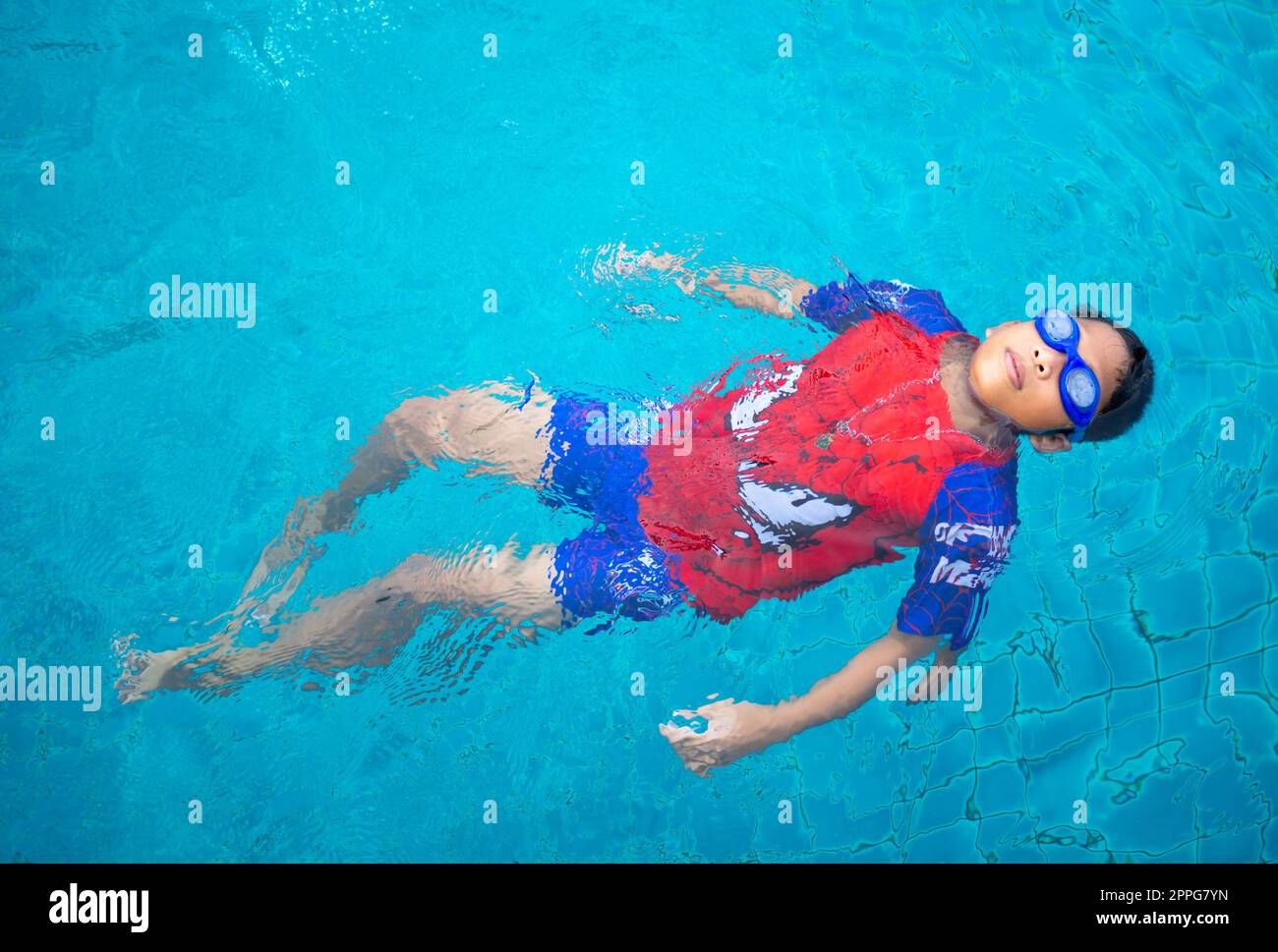 garçon portant un maillot de bain et des lunettes nageant au milieu de la piscine avec un fond bleu Banque D'Images