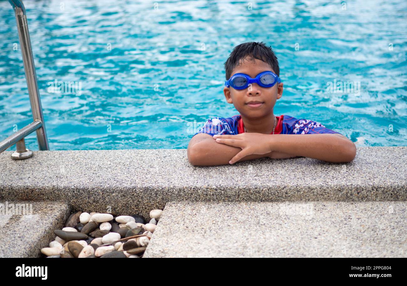 Le garçon portant des maillots de bain et des lunettes Smile tout en étant perché sur le bord de la piscine. Banque D'Images