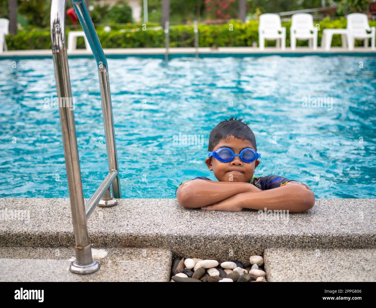 Le garçon portant des maillots de bain et des lunettes Smile tout en étant perché sur le bord de la piscine. Banque D'Images