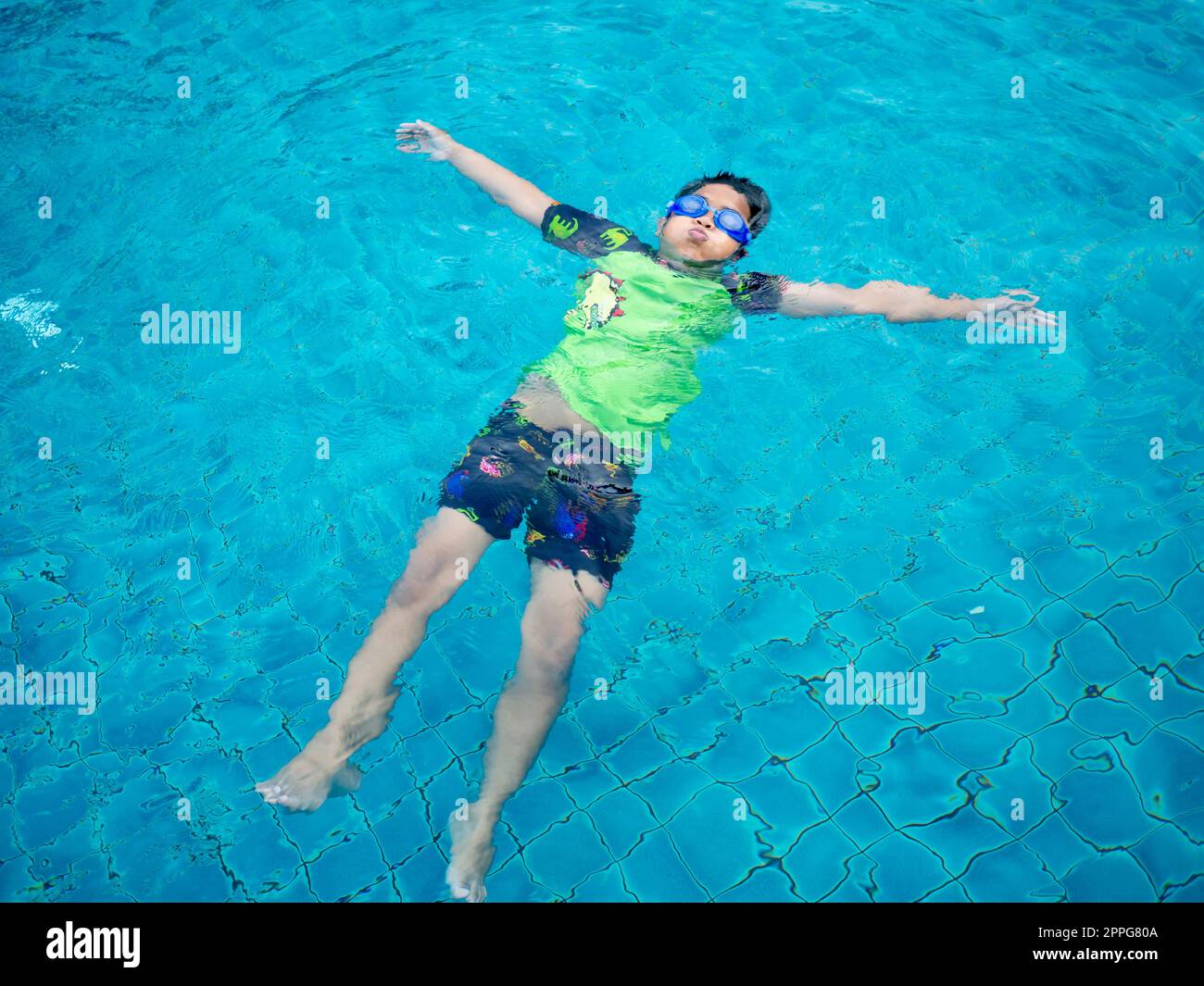 garçon portant un maillot de bain et des lunettes nageant au milieu de la piscine avec un fond bleu Banque D'Images