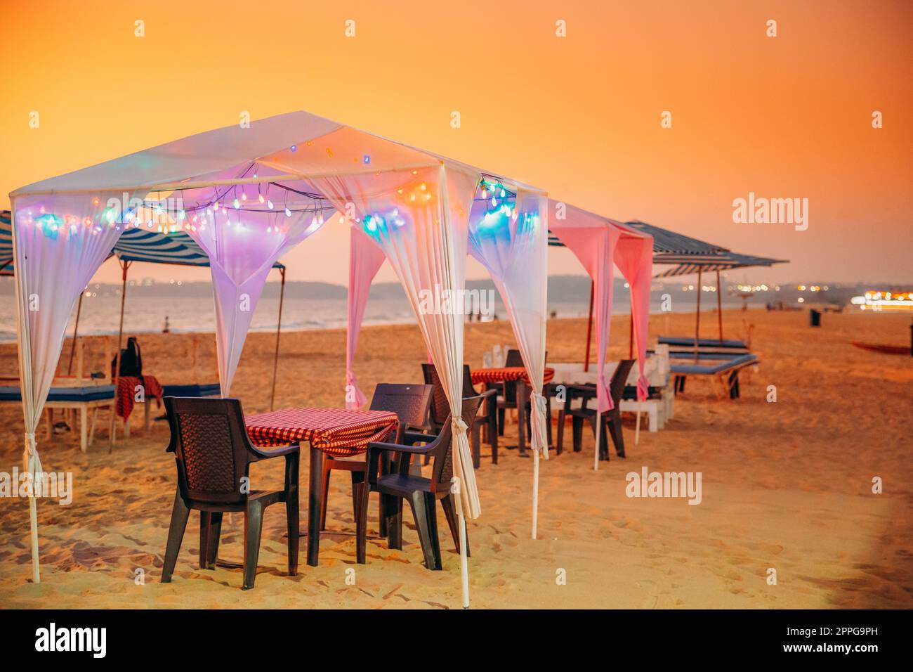 Goa, Inde. Tentes gazebo avec lampe pour les touristes sur la plage avec tables et chaises à l'intérieur au coucher du soleil Banque D'Images