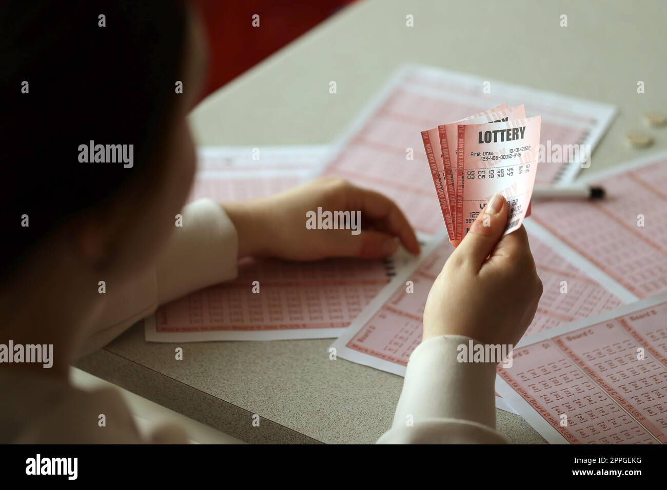 Remplir un billet de loterie. Une jeune femme tient le billet de loterie avec une rangée complète de numéros sur le fond des feuilles vierges de loterie. Banque D'Images