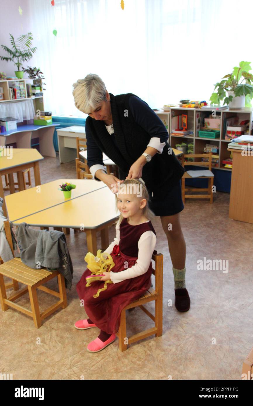 l'enseignant fait la coiffure pour l'enfant à la maternelle. le professeur tresse les tresses Banque D'Images