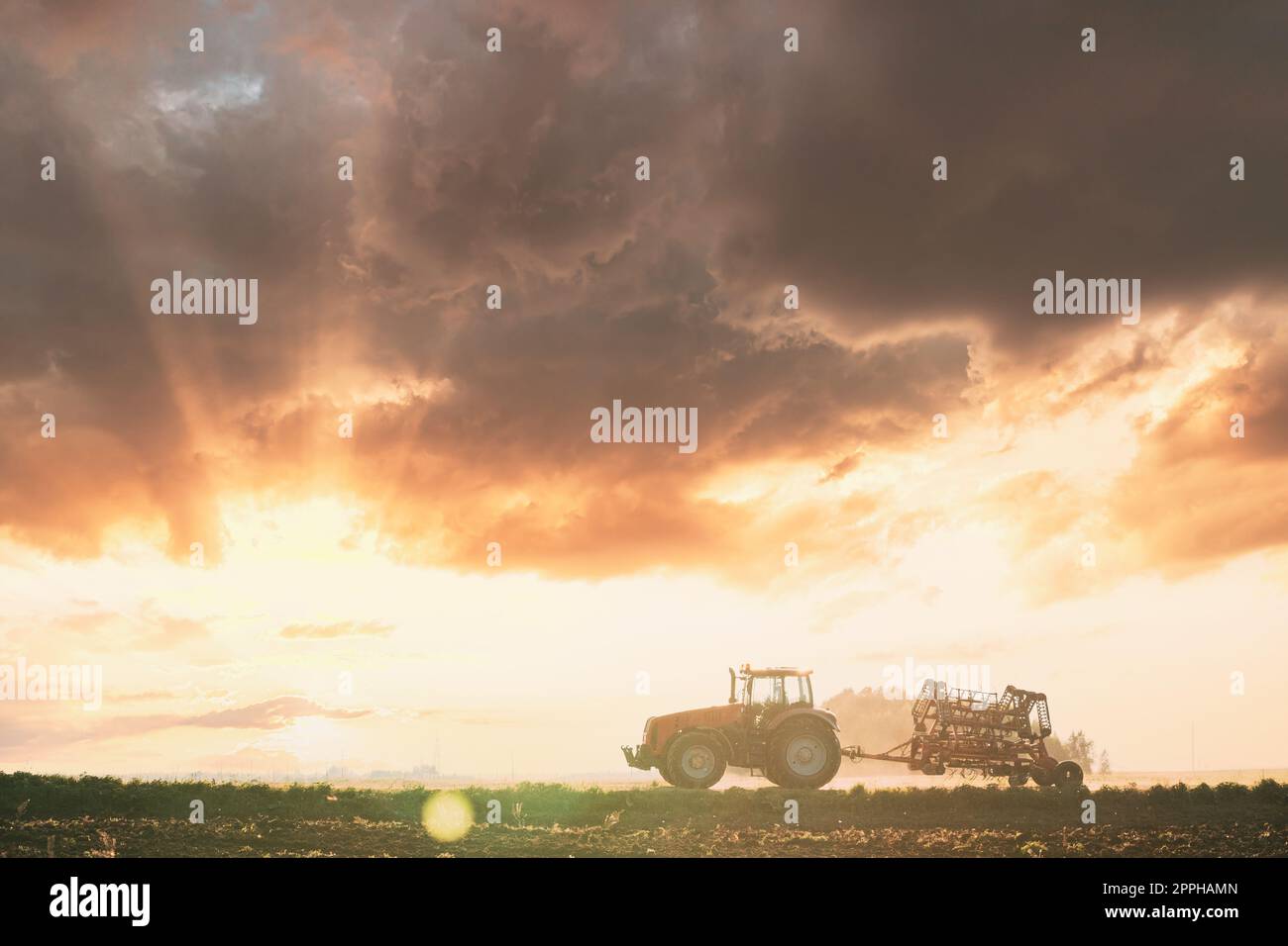 Tracteur sur route au printemps. Début de la saison agricole du printemps. Cultivateur monté sur tracteur en campagne rurale. Sunny Spring Sunset Sunrise Sky Banque D'Images