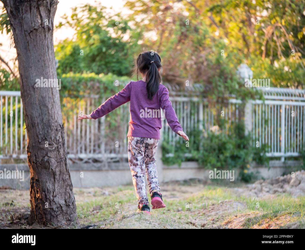 Joyeux enfant, asiatique bébé enfant fille marche dans le jardin, lumière de coucher de soleil, arrière côté, essayer d'équilibrer le corps à la main Banque D'Images