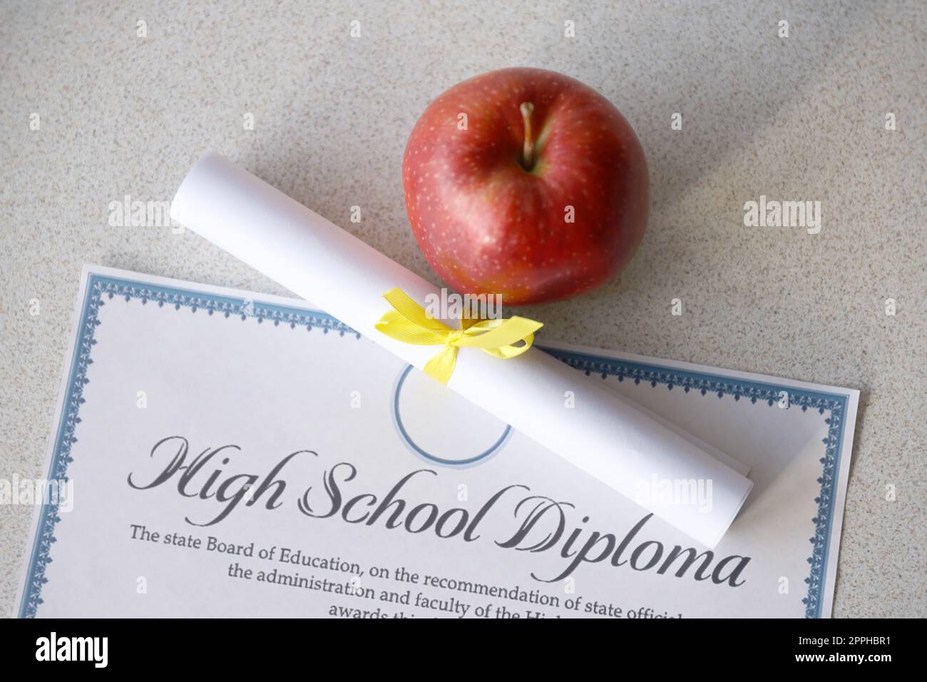 Un diplôme d'études secondaires repose sur la table avec un petit rouleau et une pomme rouge. Documents éducatifs Banque D'Images