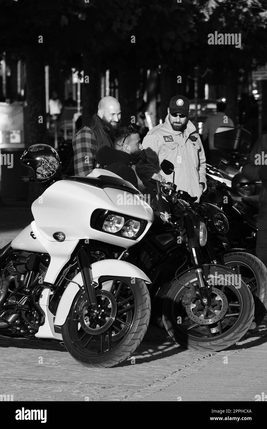 Échelle de gris verticale de trois mâles debout par une moto à hacheur blanc. Harley Davidon à Düsseldorf, Allemagne. Banque D'Images