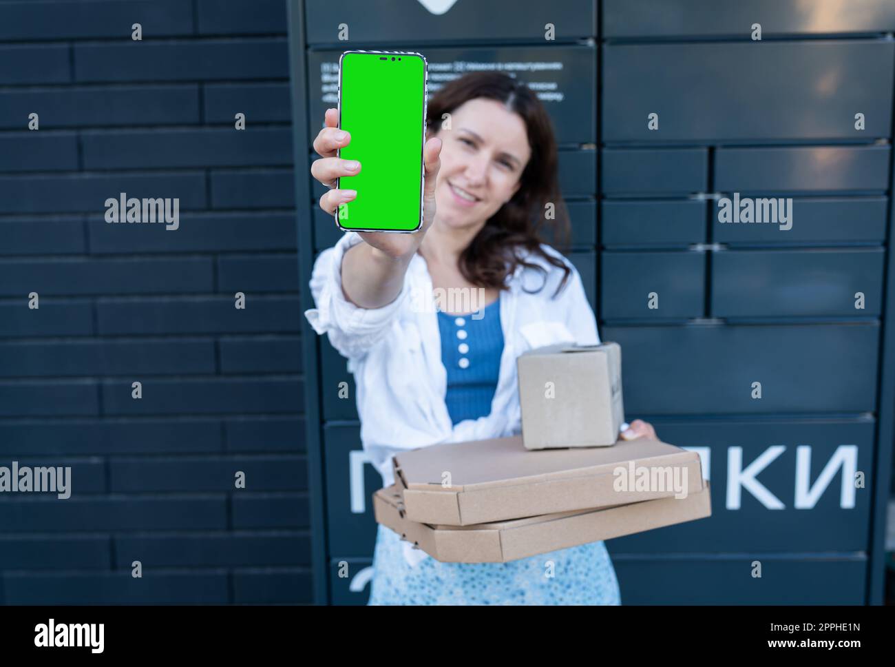 Femme heureuse tenant le téléphone portable avec maquette d'écran vert pour l'inscription et tenant de nombreuses boîtes en carton différentes avec commande en ligne, satisfaite de la livraison rapide, achetant des produits de haute qualité. Banque D'Images