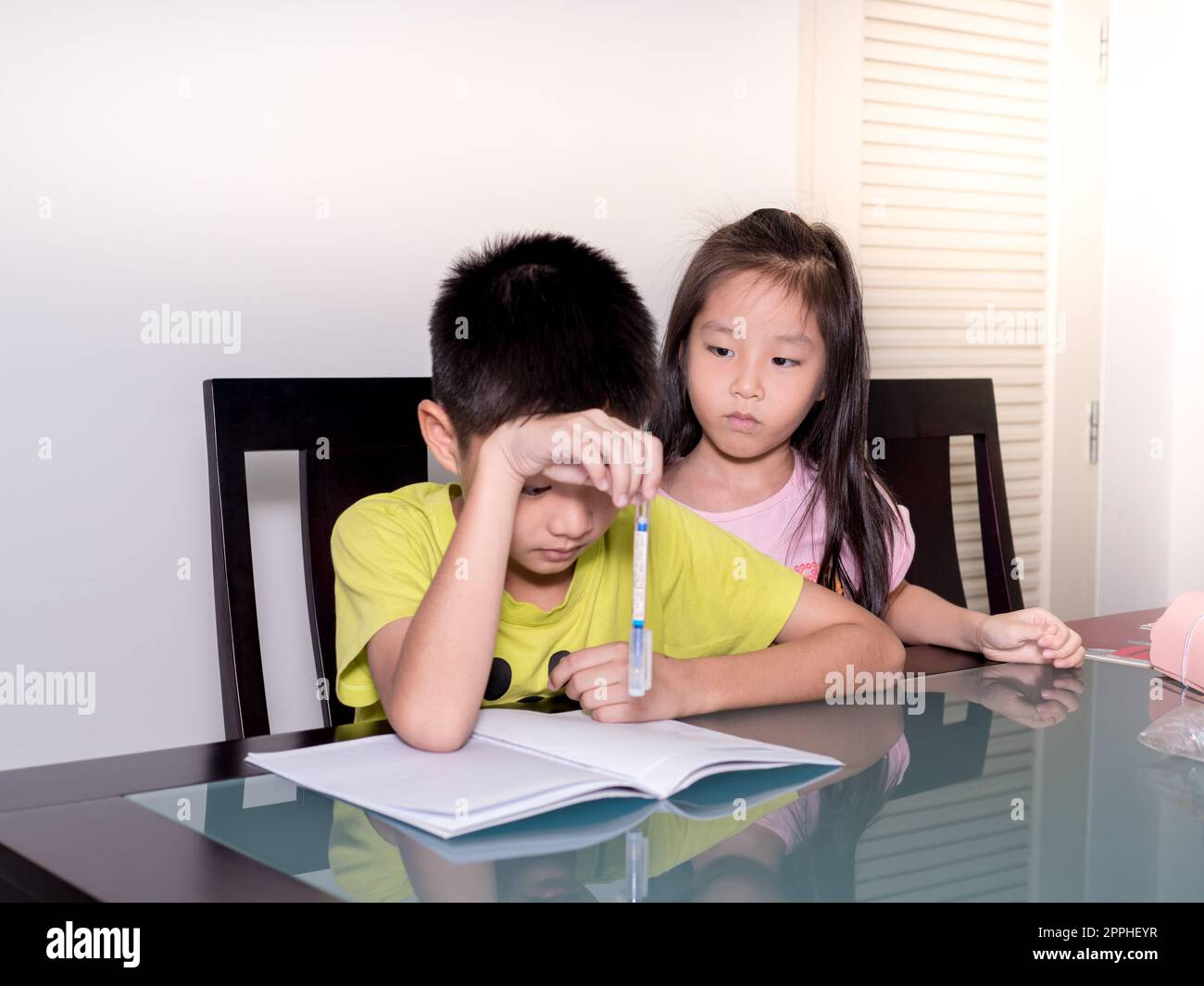 Asie petite sœur regarde son frère étudier et faire ses devoirs à la maison, sur la table, l'éducation à la maison, la pensée action Banque D'Images