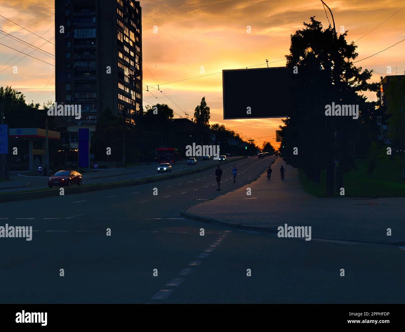 Paysage urbain et coucher de soleil en soirée. coucher de soleil dans la rue avec des adolescents sur des planches à roulettes et des vélos Banque D'Images