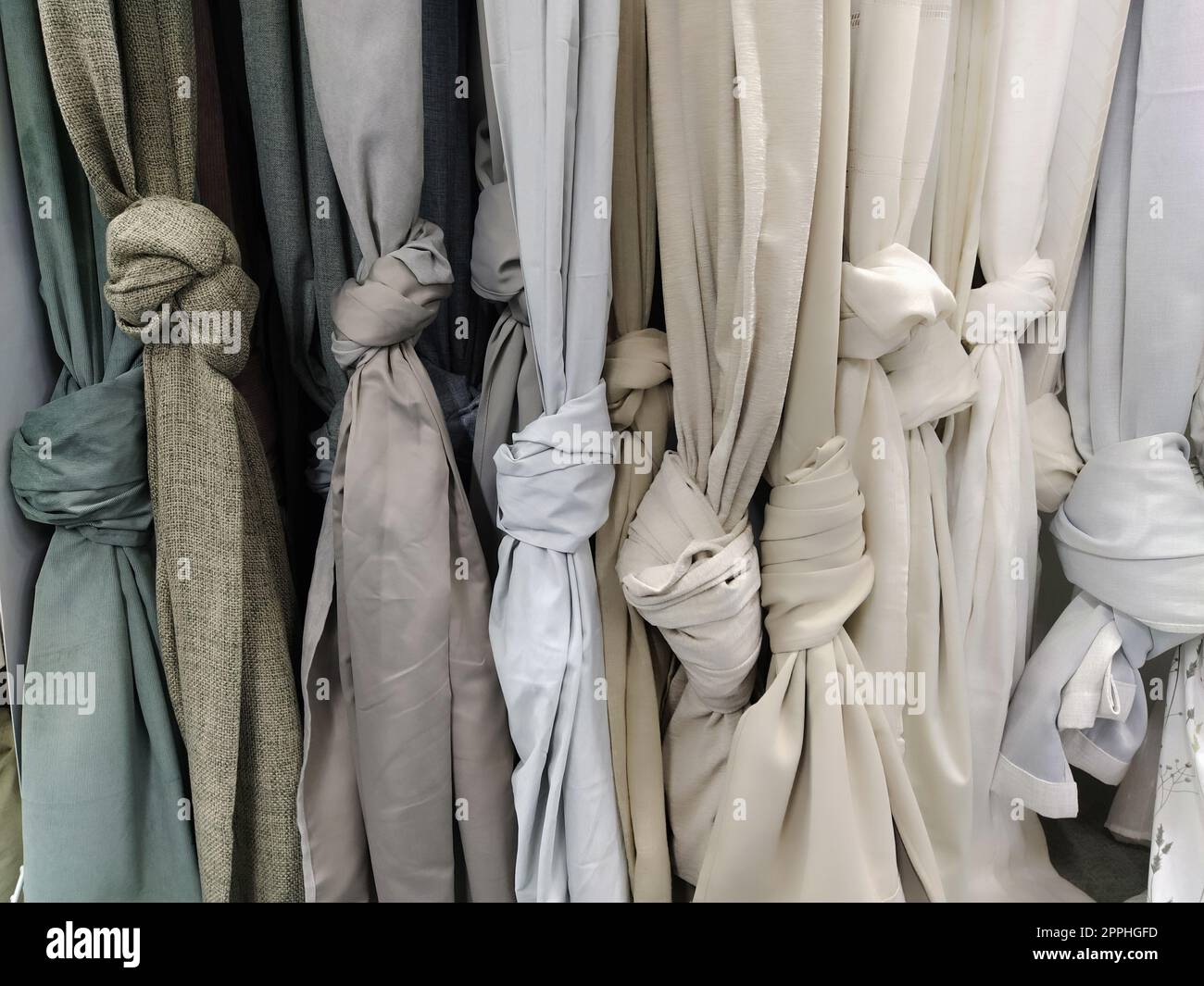 Rideau et tissu pour draperie et décoration intérieure. Des échantillons de tissus gris et blancs dans le magasin sont suspendus verticalement et noués en nœuds. Rideaux dans la vitrine. Banque D'Images