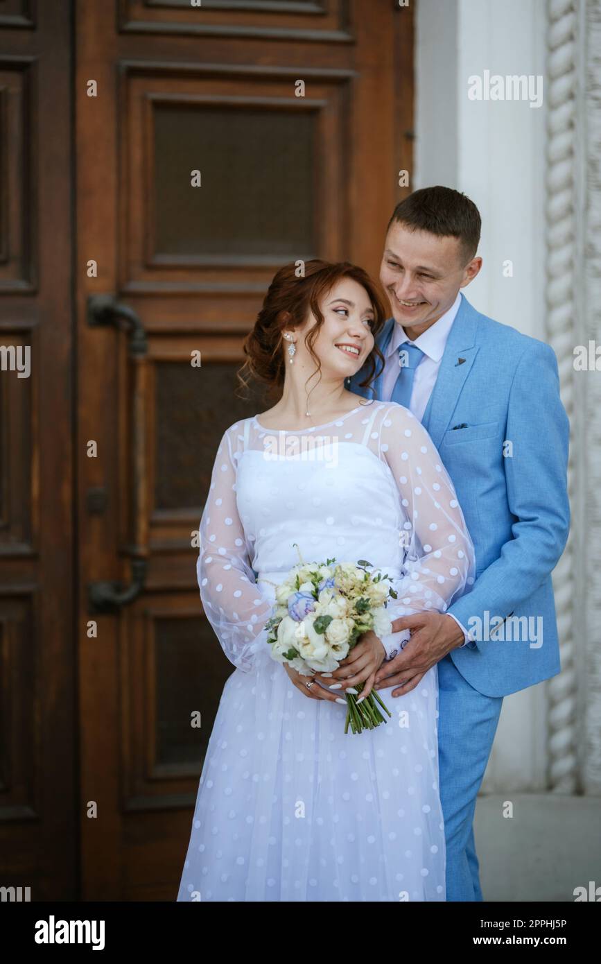 mariée dans une robe de mariage légère avec un bouquet à côté du marié dans  un costume bleu Photo Stock - Alamy