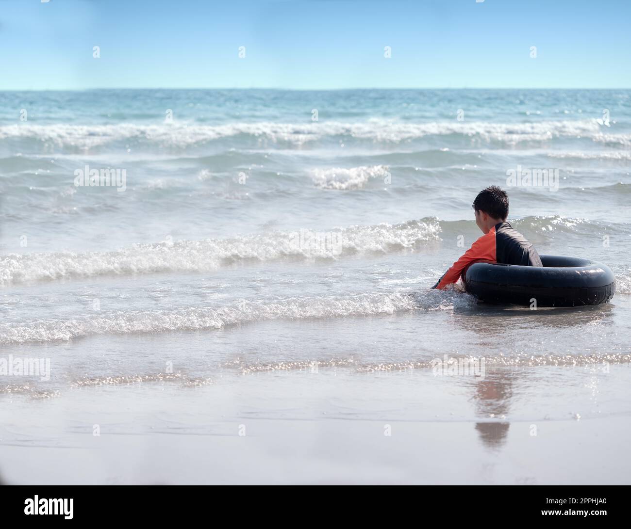 Un petit garçon asiatique joue des vagues sur la plage, avec une bouée de sauvetage Banque D'Images