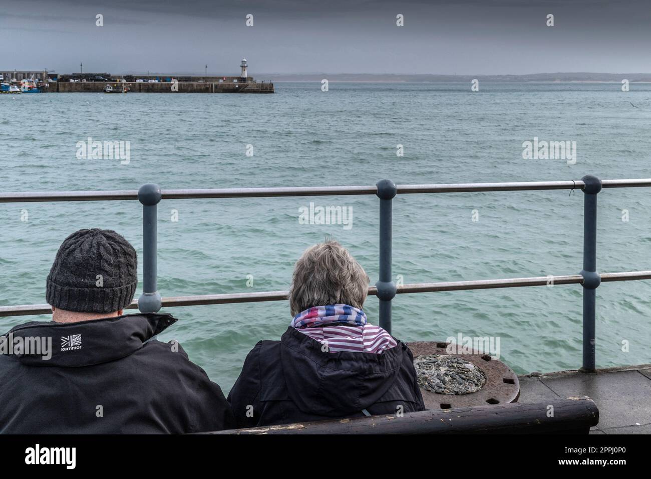 Météo au Royaume-Uni. Un couple assis sur un banc donnant sur Smeatons Pier lors d'une journée pluvieuse et misérable dans la ville balnéaire historique de St Ives à Cornwa Banque D'Images