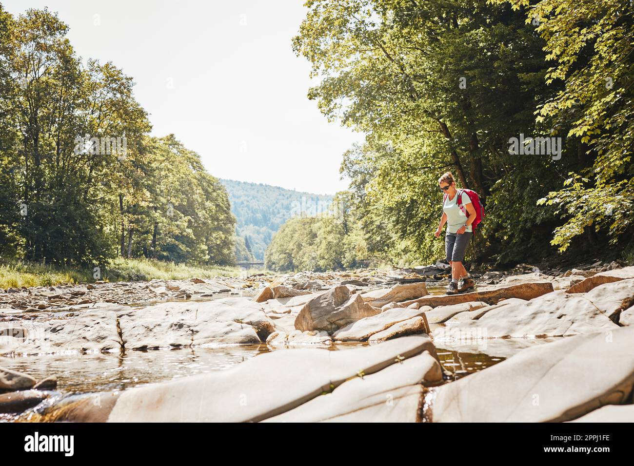 Trekking avec l'image concept de sac à dos. Une femelle Backpacker portant des bottes de randonnée traversant la rivière de montagne. Femme randonnée dans les montagnes pendant le voyage d'été. Banque D'Images
