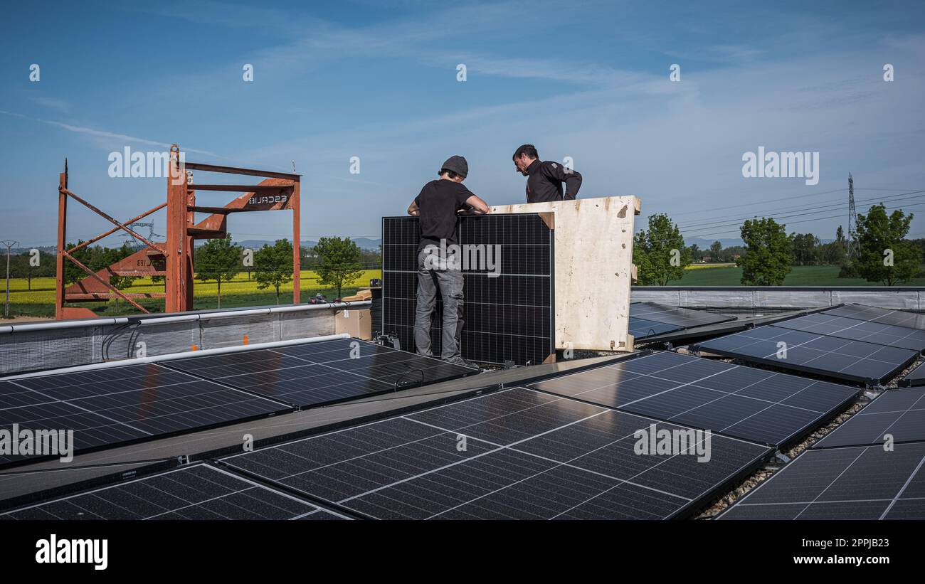 Ingénieurs de l'équipe masculine installant un système autonome de panneau solaire photovoltaïque. Électriciens montant le module solaire bleu sur le toit de la maison moderne. Concept d'énergie alternative Banque D'Images