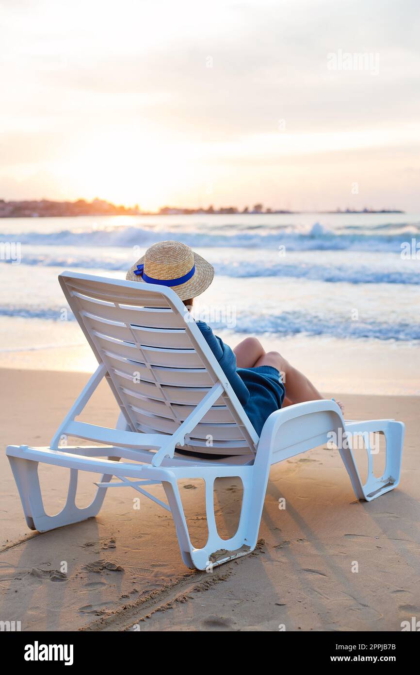 Belle fille dans un chapeau est assise sur un transat, l'aube de la réunion Banque D'Images