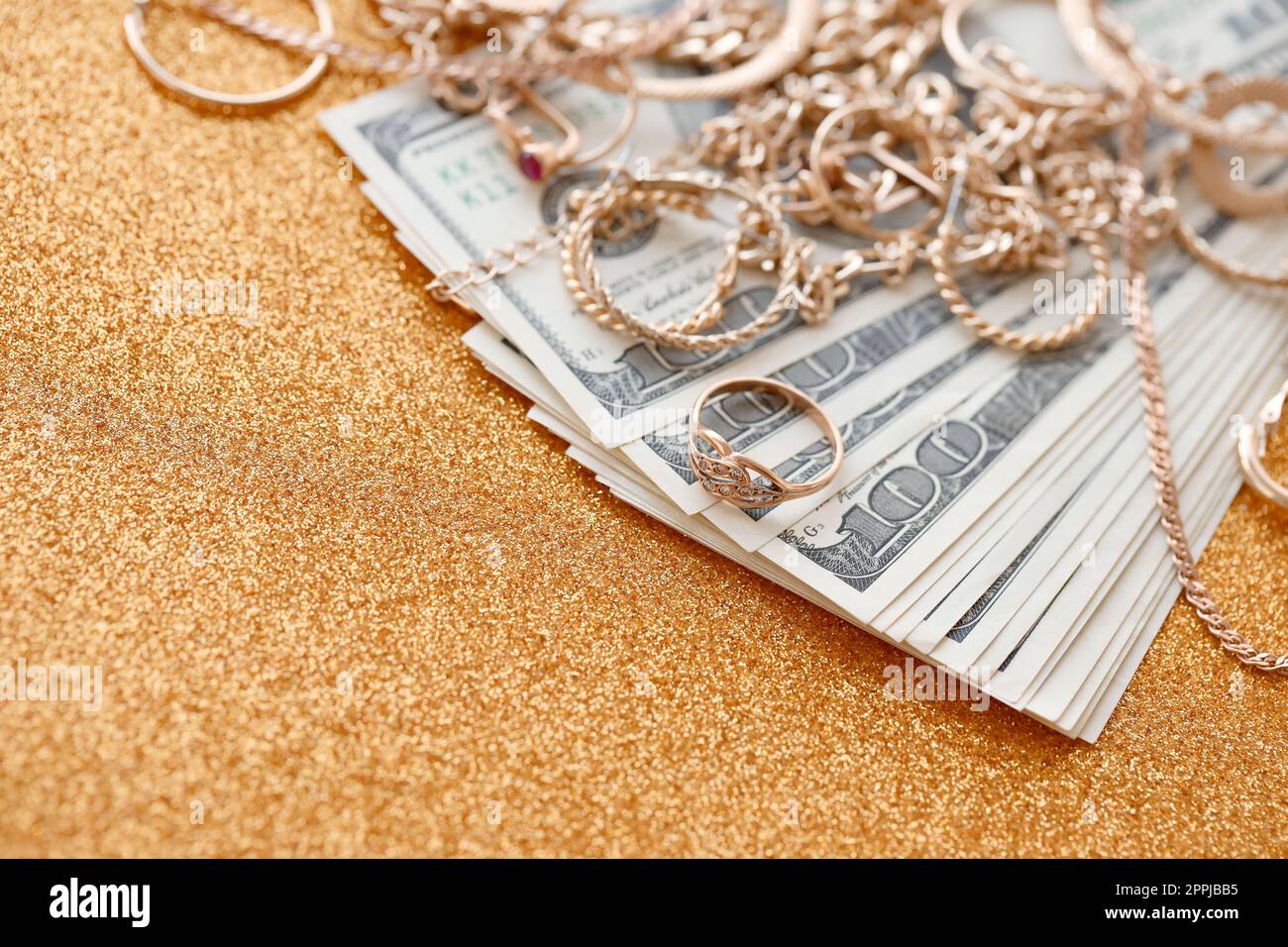 Beaucoup de bagues de bijoux en or coûteux, boucles d'oreilles et colliers avec une grande quantité de billets de dollar US sur la surface de fond dorée de paillettes de luxe. Prêteur sur gage ou bijouterie Banque D'Images