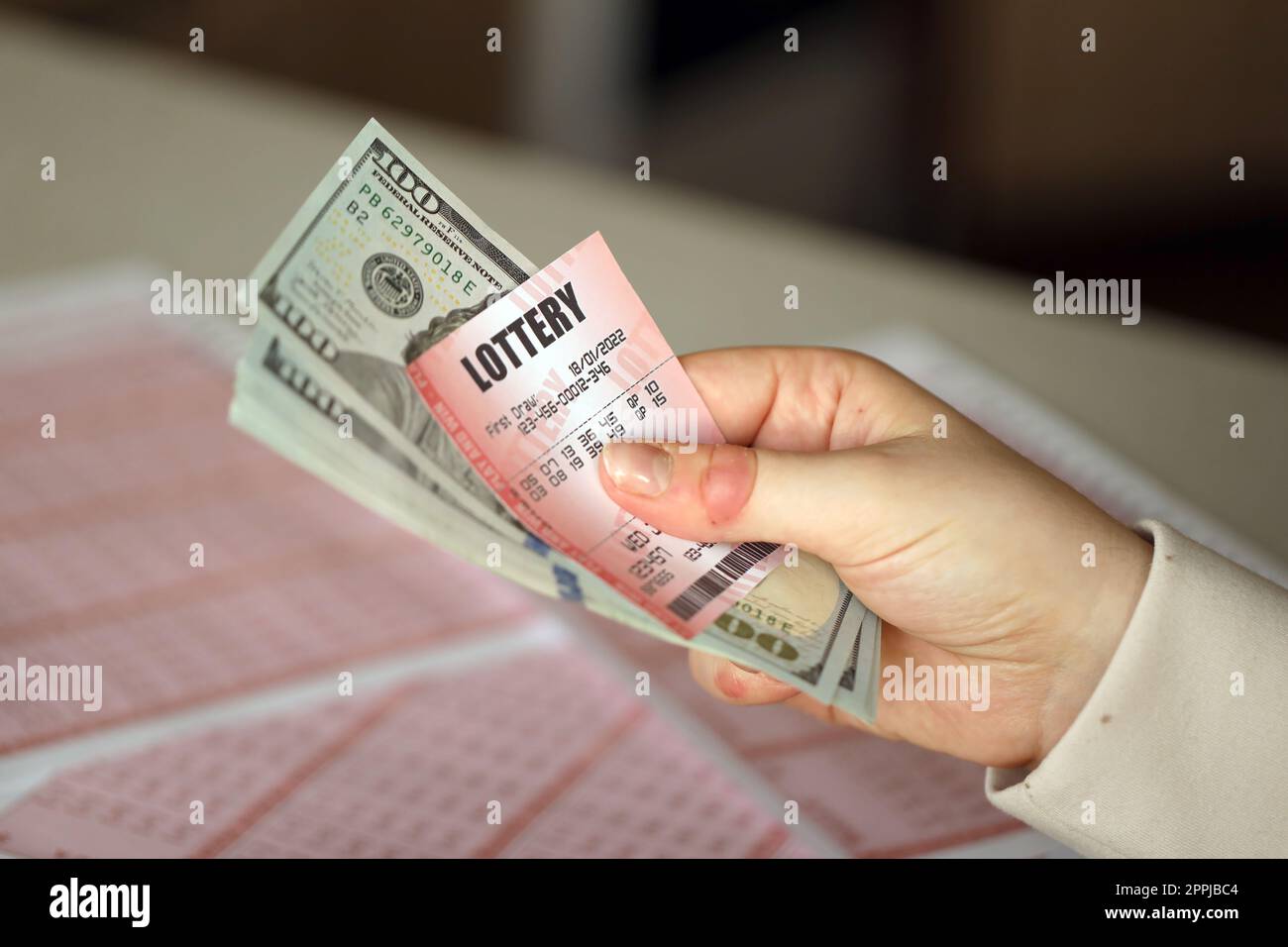 Une jeune femme tient le billet de loterie avec une rangée complète de chiffres et de billets de dollar sur le fond des feuilles vierges de loterie Banque D'Images