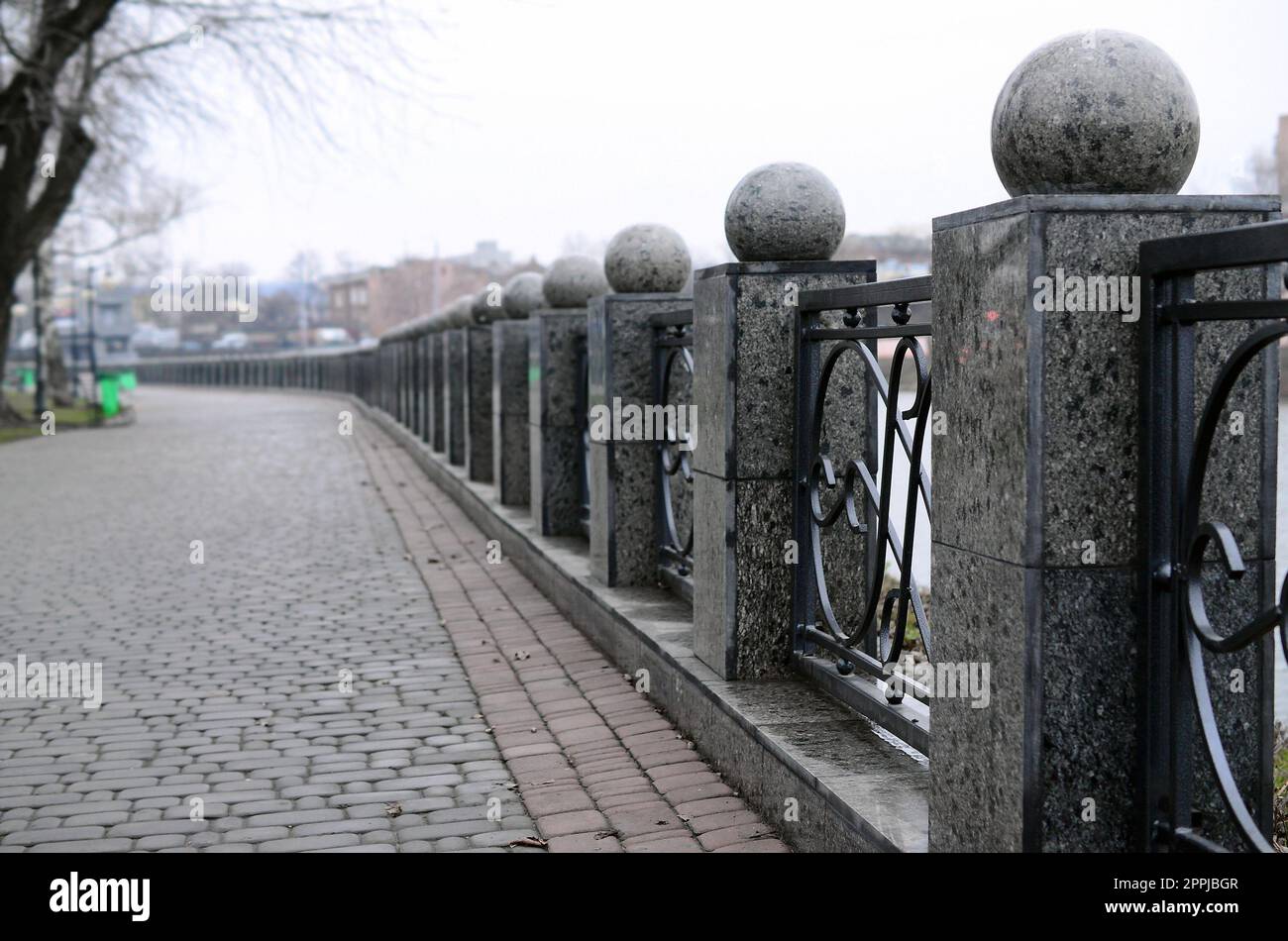 Une belle clôture en granit avec des sections en métal forgé et des boules décoratives comme décorations. La clôture est construite le long du remblai de la rue Banque D'Images