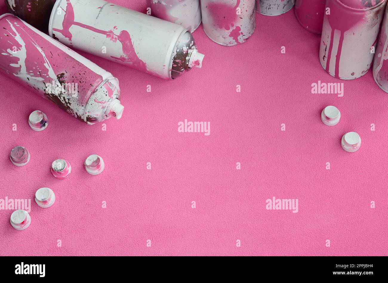 Certains aérosols roses usagés et des buses avec des gouttes de peinture reposent sur une couverture de tissu molletonné rose pâle doux et poilu. Couleur de conception féminine classique. Concept de hooliganisme graffiti Banque D'Images