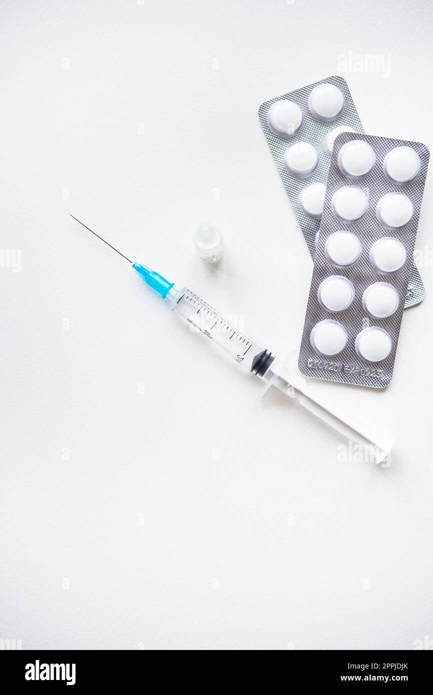 Préparation pour la vaccination contre le covid-19. Seringue, vaccin, pilules, masque médical sur une table blanche. Banque D'Images