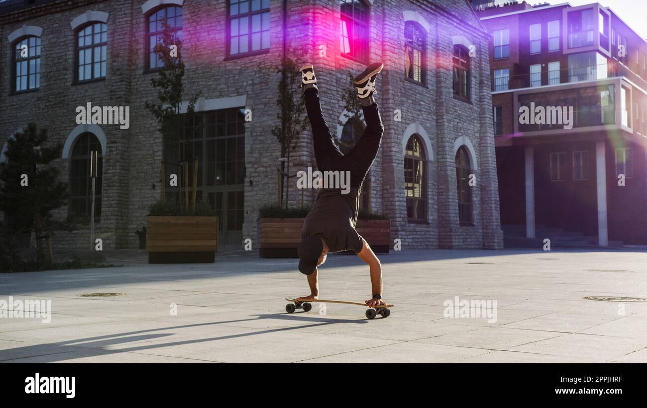 Le patineur professionnel agile se tient sur les mains de son skateboard. Un homme fort qui fait des poussettes sur une planche à repasser. À l'arrière-plan, un modèle à la mode Banque D'Images