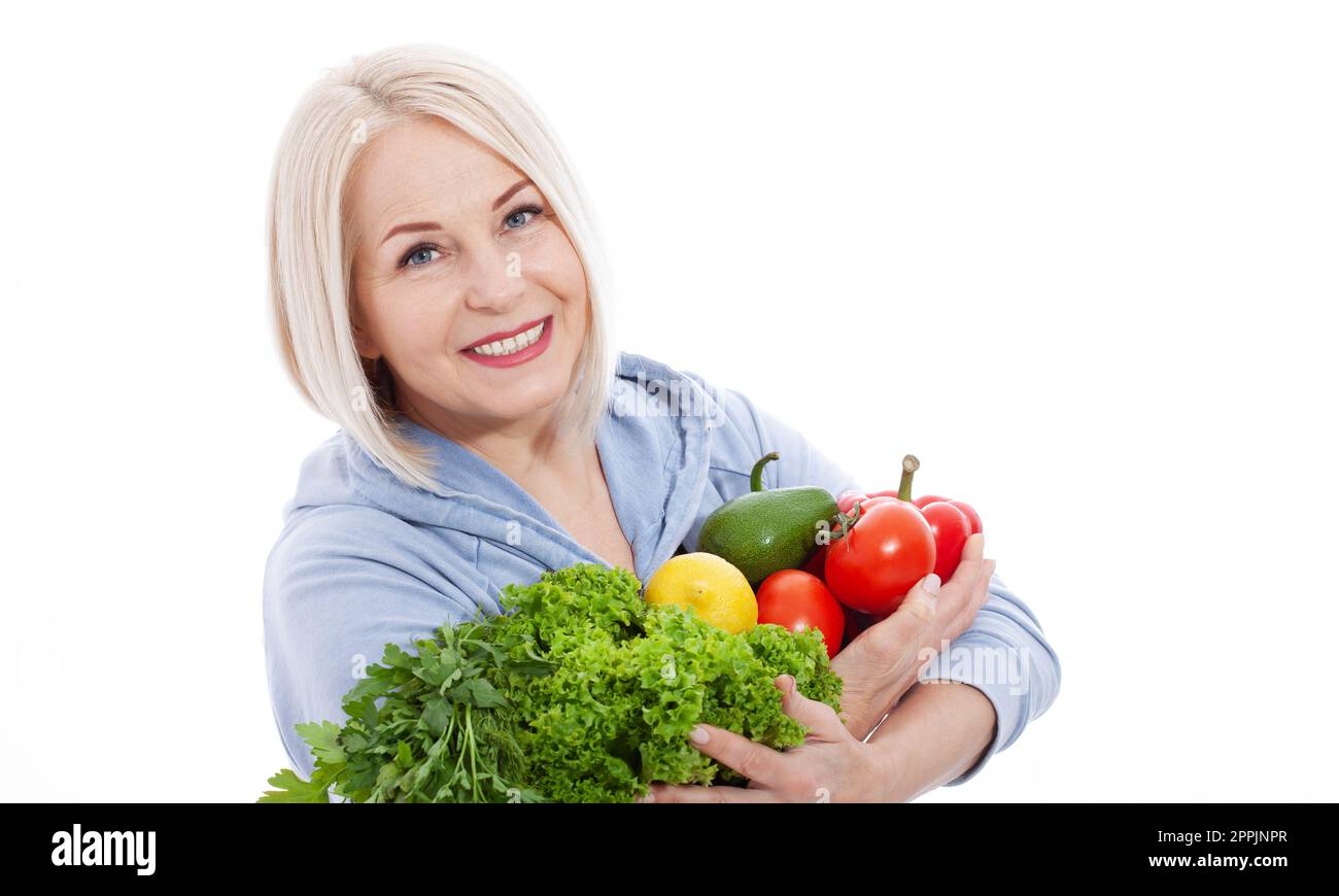 Une femme heureuse avec des cheveux blonds et un beau sourire tient un poivron rouge et une laitue verte de légumes et d'herbes dans ses mains pour une alimentation saine. Le concept Banque D'Images