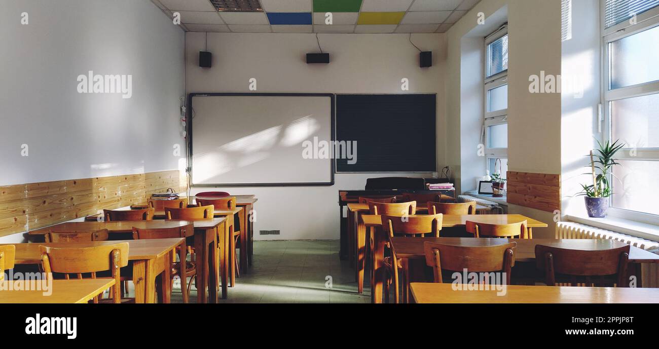 Musique solfège classe vide à l'école. Les rayons du soleil tombent sur le sol par la fenêtre. Tables et chaises en bois pour étudiants. Conseil scolaire et murs blancs. Intérieur de l'école. Banque D'Images
