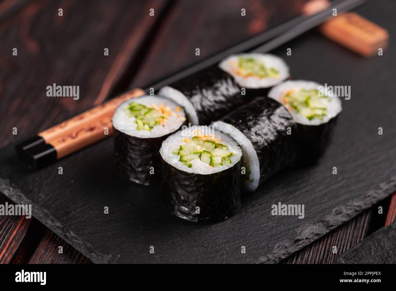 Gros plan sur un rouleau de sushis Maki au concombre et au sésame avec baguettes. Menu sushi. Cuisine japonaise. Banque D'Images