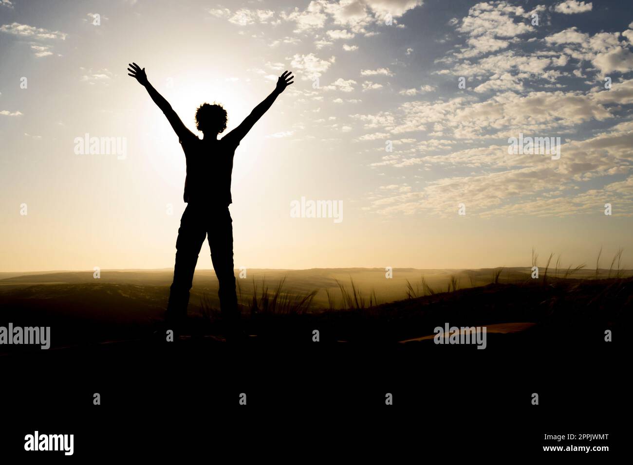 Silhouette de personne debout sur une dune au lever du soleil, bras en l'air. Banque D'Images