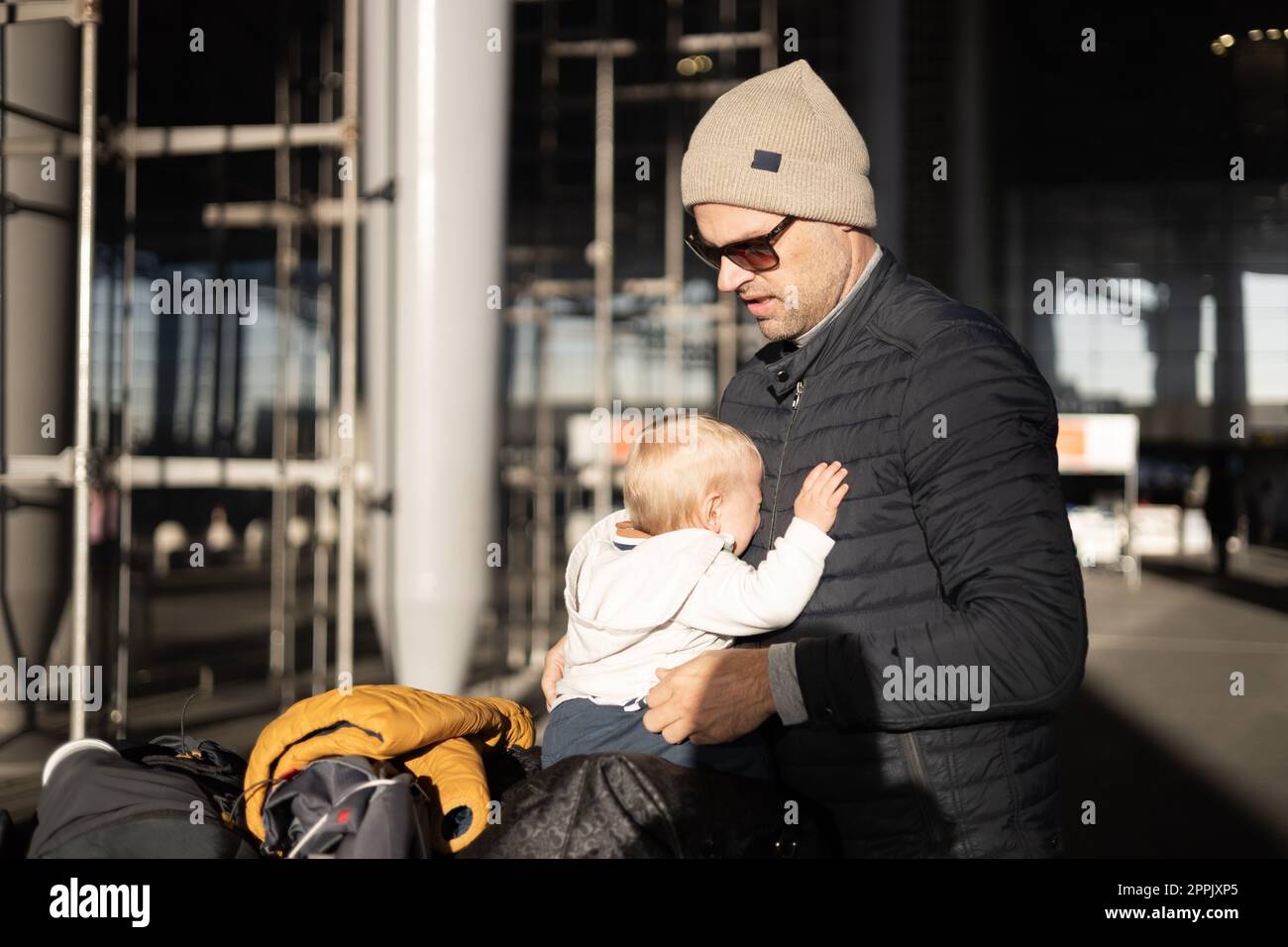 Fatherat réconfortant son bébé bébé garçon en pleurs enfant fatigué assis sur le dessus du chariot à bagages en face de la gare de l'aéroport tout en voyageant avec la famille. Banque D'Images