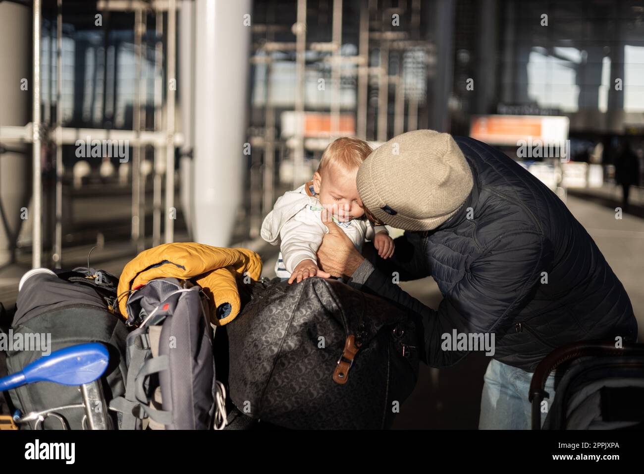 Fatherat réconfortant son bébé bébé garçon en pleurs enfant fatigué assis sur le dessus du chariot à bagages en face de la gare de l'aéroport tout en voyageant avec la famille. Banque D'Images