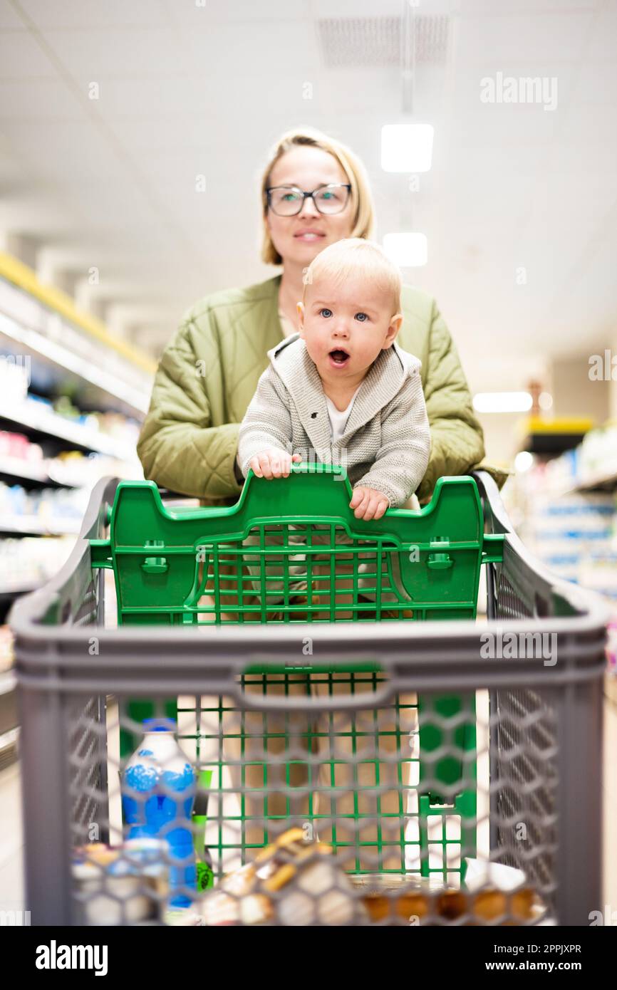 Mère poussant le chariot avec son bébé garçon enfant dans l'allée du rayon dans l'épicerie du supermarché. Concept shopping avec enfants. Banque D'Images