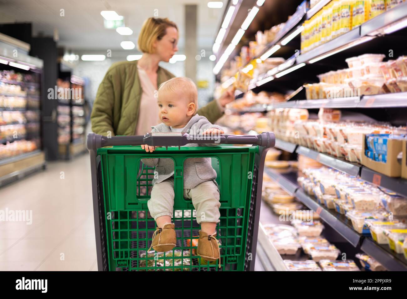 Mère poussant le chariot avec son bébé garçon enfant dans l'allée du rayon dans l'épicerie du supermarché. Concept shopping avec enfants. Banque D'Images