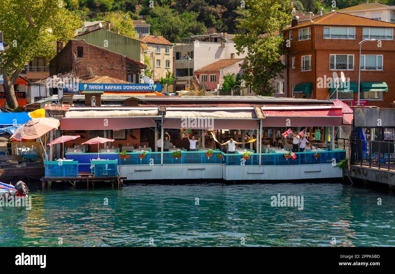 Le personnel flottant du restaurant agitant des drapeaux pour accueillir les visiteurs d'Anadolu Kavagi, dans le détroit du Bosphore, Istanbul, Turquie Banque D'Images