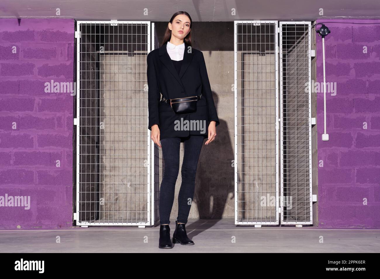 Fille en veste noire et jeans debout près de la salle technologique avec porte en grille métallique Banque D'Images