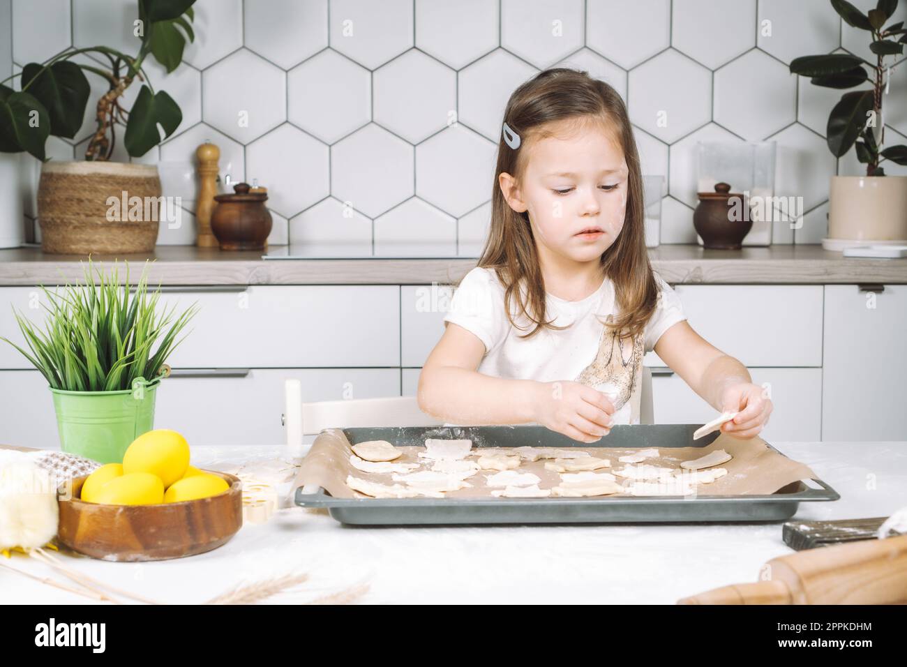 Portrait de petite fille studieusement enfant, chaise assise cuisine, faire différents biscuits de pâte de forme de pâques, poêle à égoutter Banque D'Images