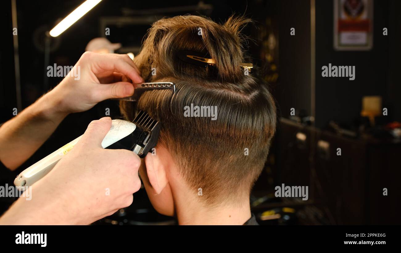 coiffure pour hommes et coupe de cheveux avec tondeuse à cheveux dans un salon de coiffure ou de coiffure. Service de coiffeur dans un salon de coiffure moderne dans un éclairage sombre clé avec vue arrière de lumière chaude Banque D'Images