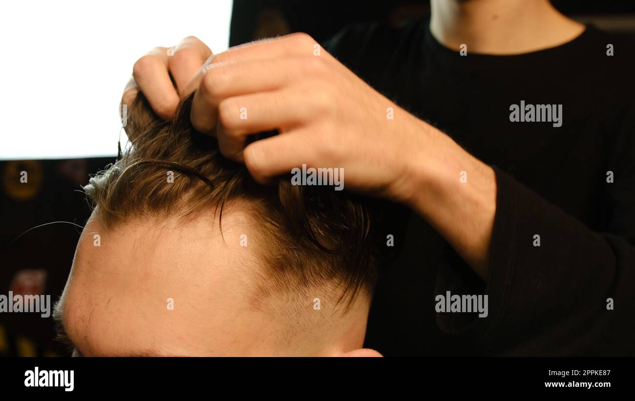 Salon de coiffure. Homme dans la chaise de barbier, coiffeur coiffant ses cheveux avec les mains dans l'éclair sombre clé. Coiffeur pour homme Banque D'Images