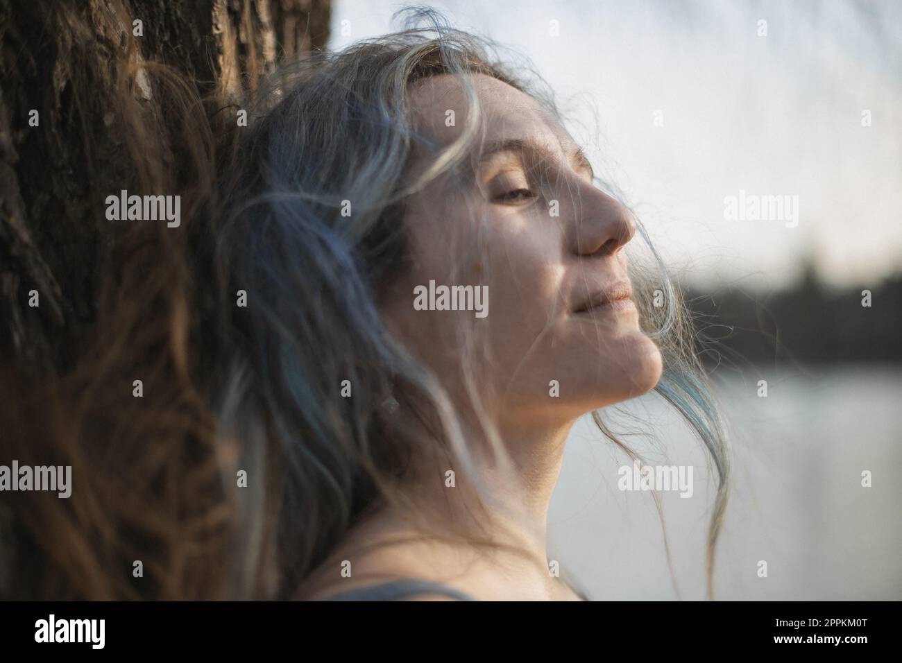Gros plan cheveux gris femme avec les yeux à moitié fermés contre l'image de portrait d'arbre Banque D'Images