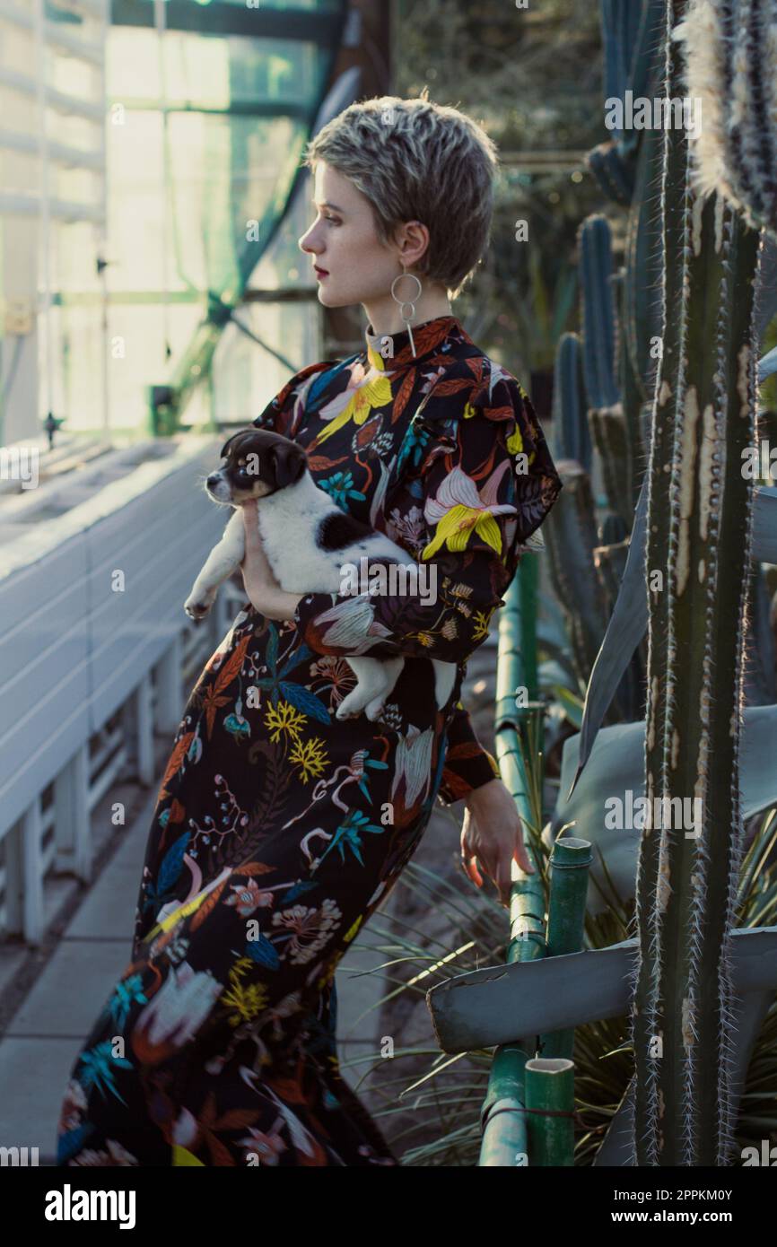Dame en robe longue tenant le chiot dans le jardin botanique photographie pittoresque Banque D'Images