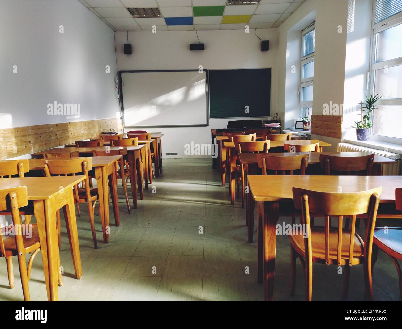 Musique solfège classe vide à l'école. Les rayons du soleil tombent sur le sol par la fenêtre. Tables et chaises en bois pour étudiants. Conseil scolaire et murs blancs. Intérieur de l'école. Banque D'Images