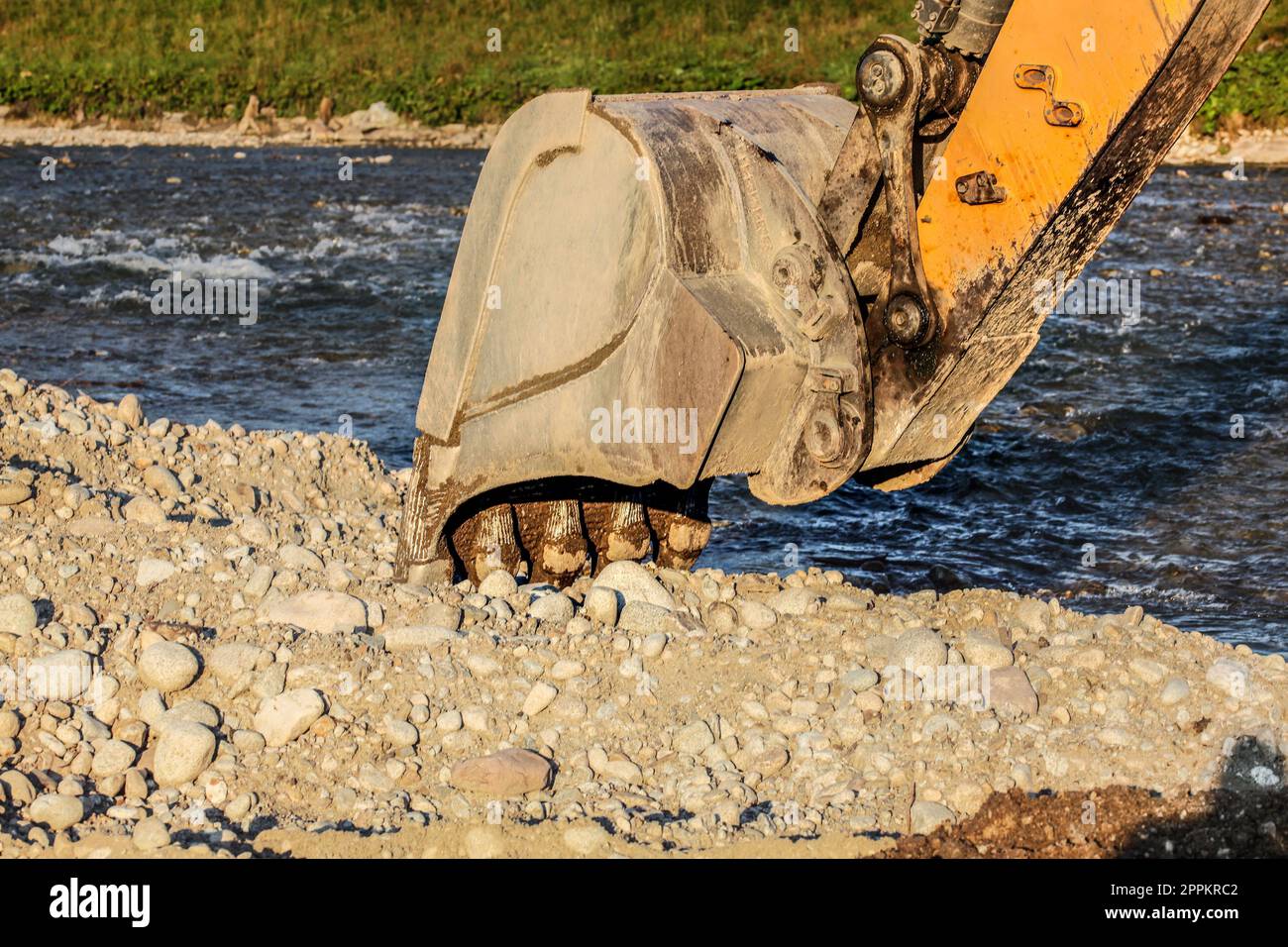 Digger excavateur jaune (machine) seau de creuser dans la masse des pierres de la rivière. Banque D'Images