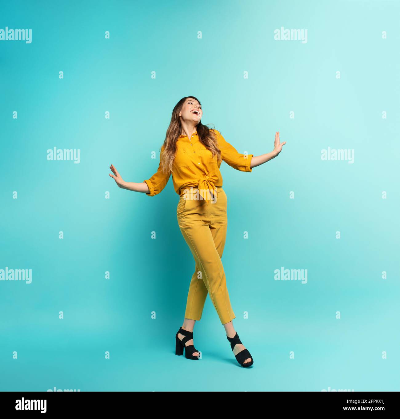 Fille brune avec un vêtement jaune marche sur un fond cyan. Concept de mode et de shopping avec expression joyeuse Banque D'Images