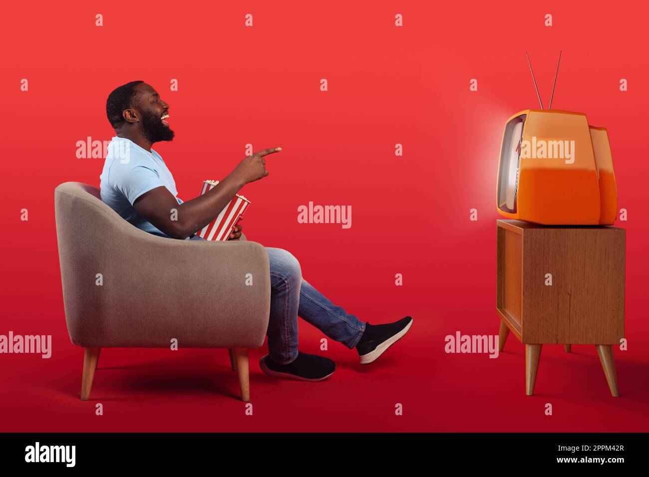 Téléspectateur amusant assis dans le fauteuil à la maison tout en mangeant des popcorns et en regardant un film sur fond rouge Banque D'Images